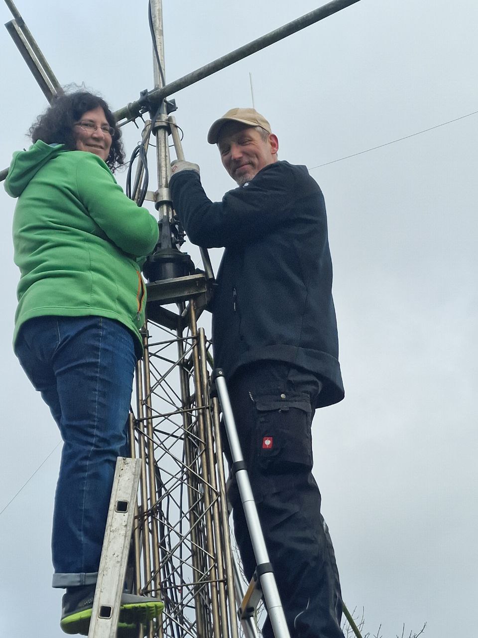 Zwei Funkamateure stehen auf einem Gittermast und montieren eine Antenne.