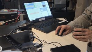 Bildschirmbild mit Anteilen Software N1MM Logger+. Hände mit Maus und Glas. Funkamateur am Computer.