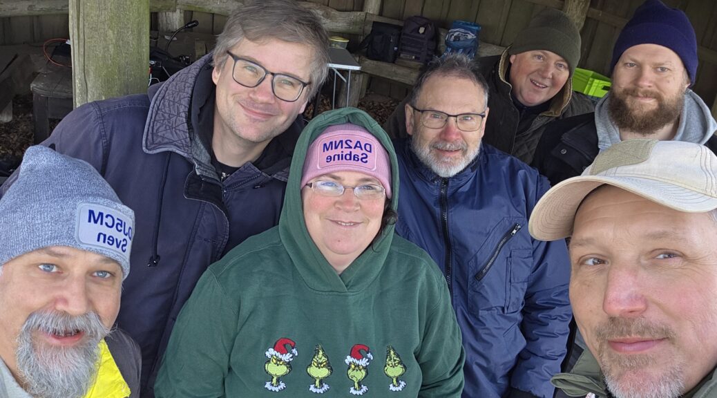 Sieben Funkamateure als Gruppenbild in der Wanderhütte Fleckeby bei einer POTA-Aktivierung.