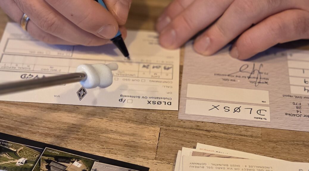 Funkamateur füllt QSL-Karten für das Clubcall DL0SX des Ortsverbands aus. Man sieht einen Stift, die Karte und seine Hände.