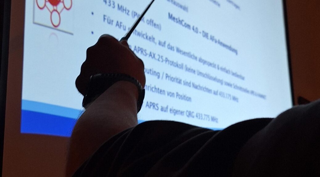 OVV Oliver DO7OMB erklärt mit einem Zeigestock die Funktion von MeshCom 4.0 an einem Beamerbild im Ruhekrug.