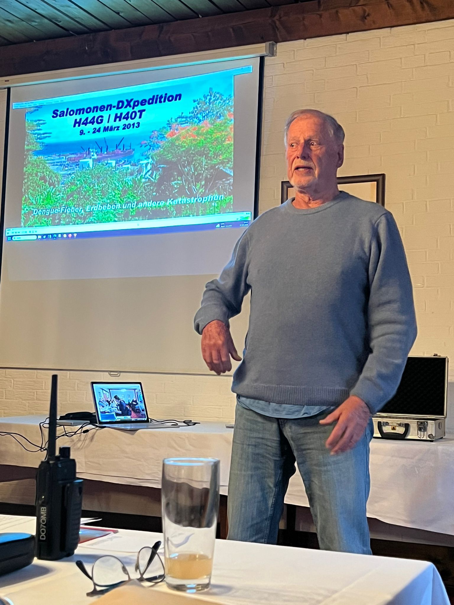 Reiner DL7KL steht vor einem Beamerbild und präsentiert sein Reisevideo.